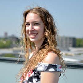 Mara lachend op haar balkon in een zomerjurk